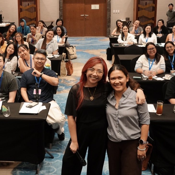 Nikki smiling with a workshop attendee, a full room of participants behind them