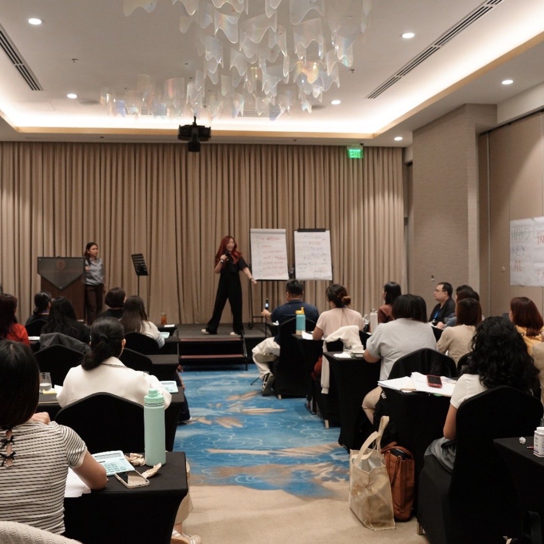 Nikki presenting at the front of a hotel ballroom workshop